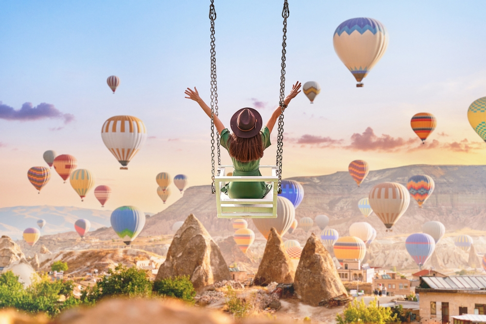 Dreaming woman swinging in Kapadokya. Flying hot air balloons in Anatolia. Happy moment life in beautiful destination in Goreme, Nevsehir