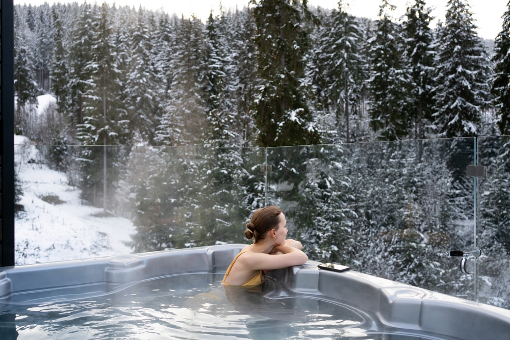 Young woman relaxing in a hot tub and thermal spa enjoying a winter view of snowy Christmas trees. Concept of recreation on hot bath and escape to nature