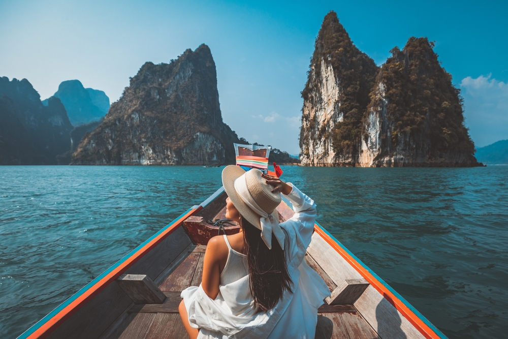 Travel summer vacation concept, Happy solo traveler asian woman with hat relax and sightseeing on Thai longtail boat in Ratchaprapha Dam at Khao Sok National Park, Surat Thani Province, Thailand