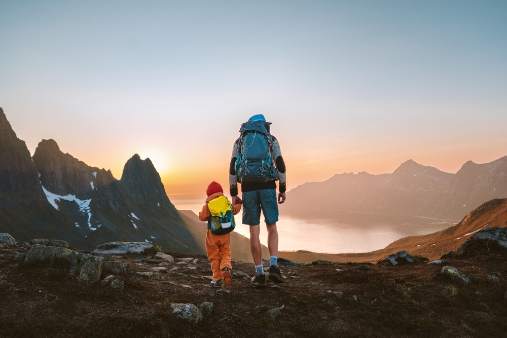 Family travel hiking adventures: father and child with backpacks in mountains of Senja island in Norway healthy lifestyle outdoor active vacations dad with kid together