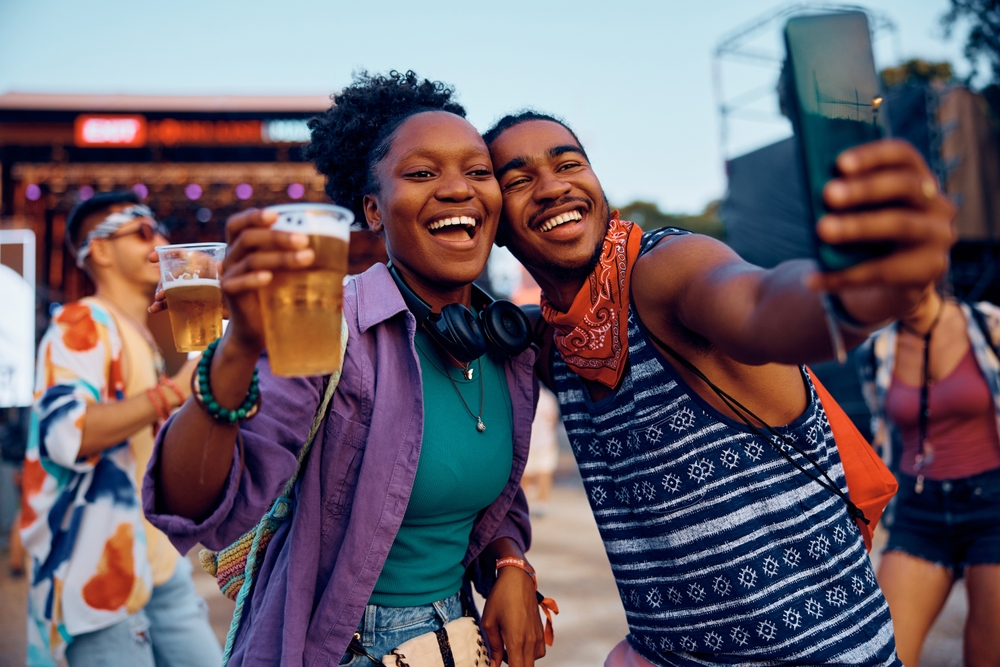 Happy African American couple having fun and taking selfie during music concert in summer.