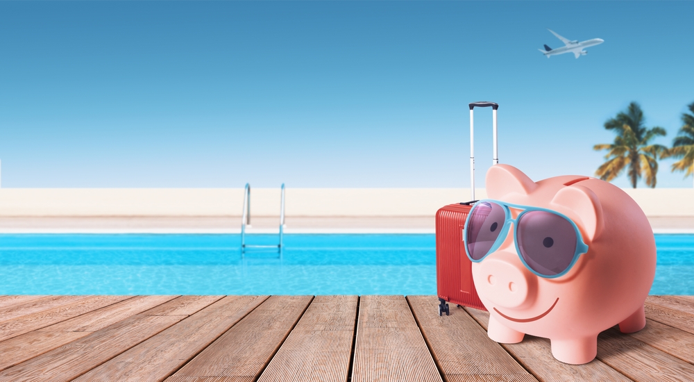 Happy piggy bank with luggage and sunglasses at the resort, cheap affordable summer vacations concept