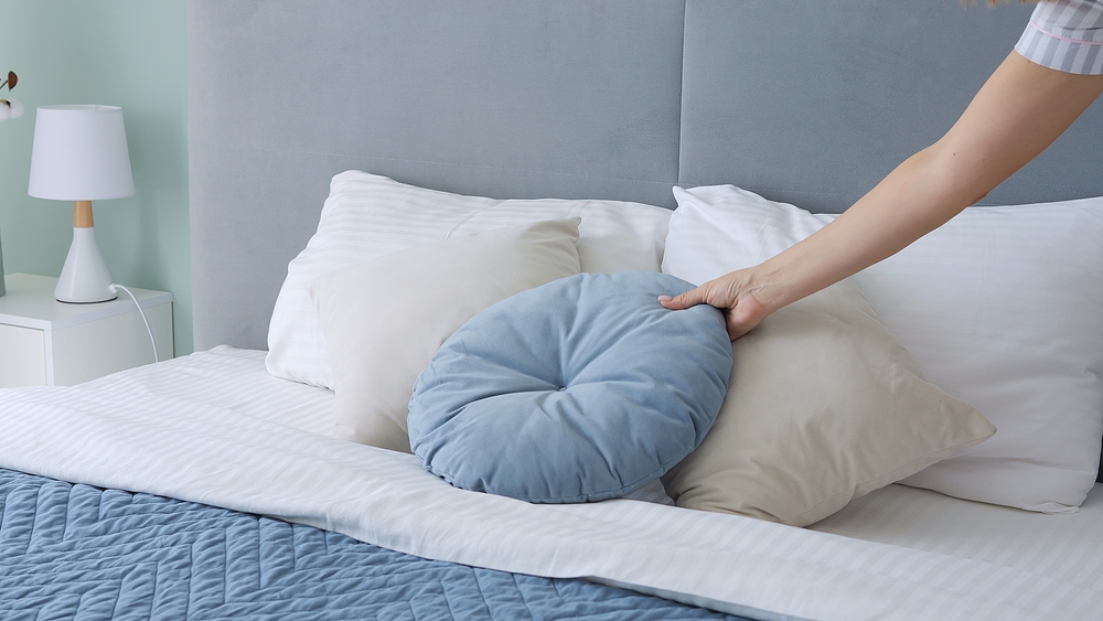 Woman arranges pillows on bed creating a cozy retreat. With each pillow placed, bed transforms into sanctuary of comfort The soft embrace of pillows invites relaxation promising peaceful night's sleep