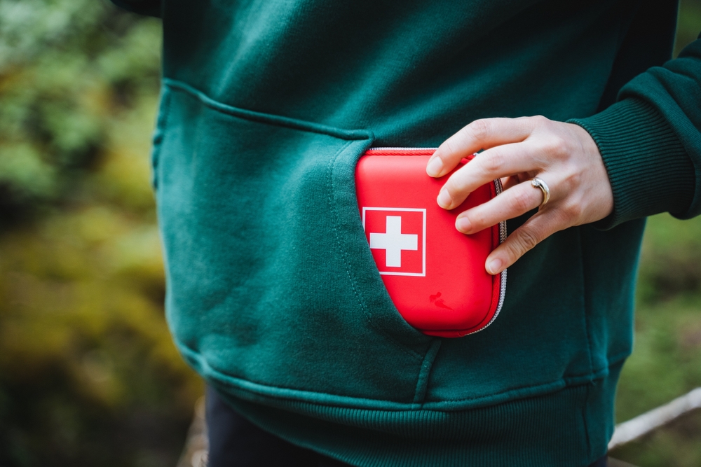 Closeup of a hand placing a first aid kit into a jacket pocket, symbolizing preparedness for emergencies, outdoor adventures, and health safety