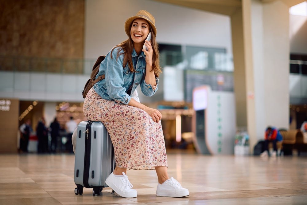 Happy female traveler talking on the phone at departure area. Copy space.