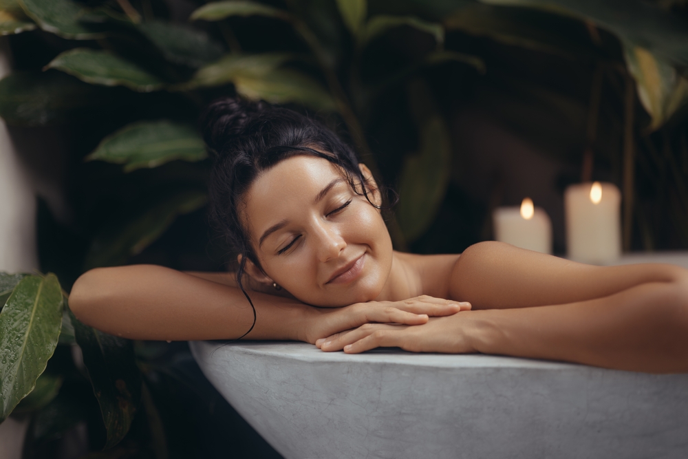 A serene woman with a relaxed expression enjoys a luxurious bath surrounded by lush greenery and soothing candlelight.