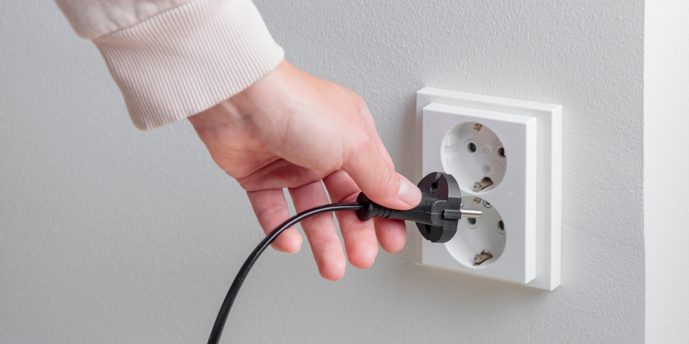 A woman's hand unplugging a power cord from an electrical outlet on a white wall.