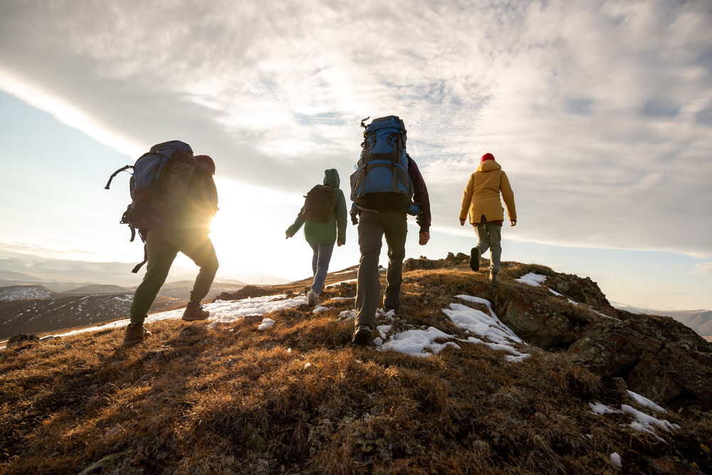 Group of four hikers with backpacks walks in mountains at sunset