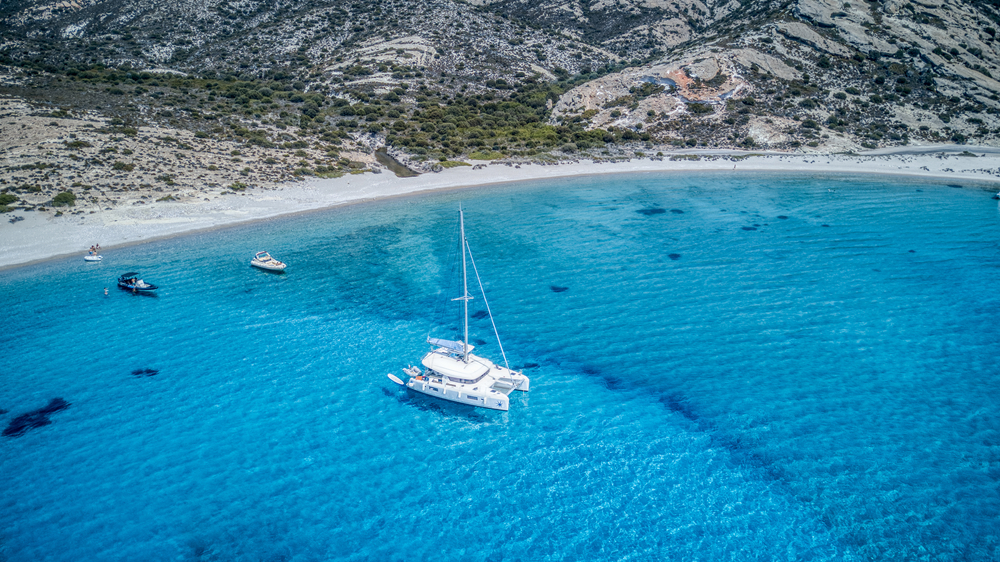 A sailing catamaran anchored in a turquoise blue bay on the uninhabited Polyaigos island