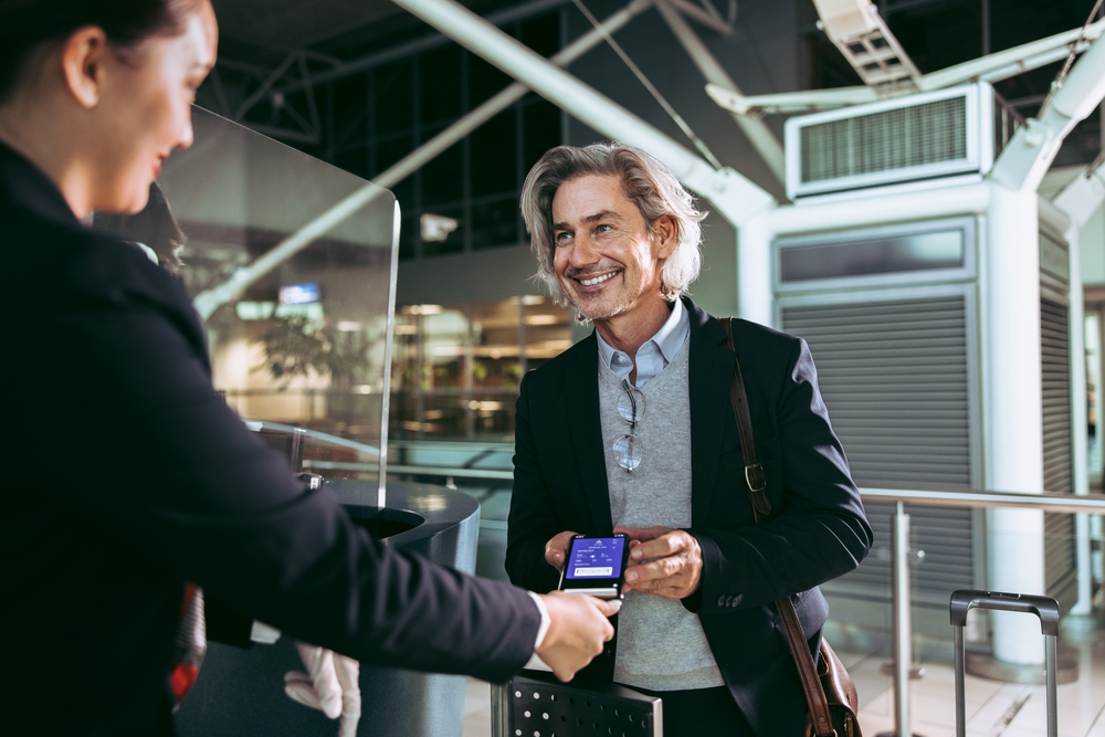 Businessman showing electronic boarding pass to flight attendant at airport check in counter.