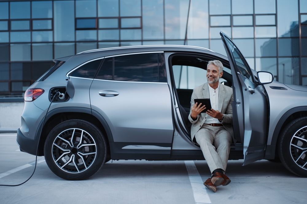 Businessman using tablet while charging car at electric vehicle charging station, close-up.