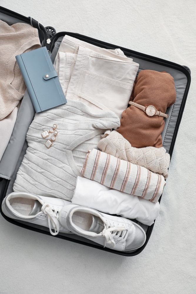 Suitcase with female clothes and accessories on white blanket