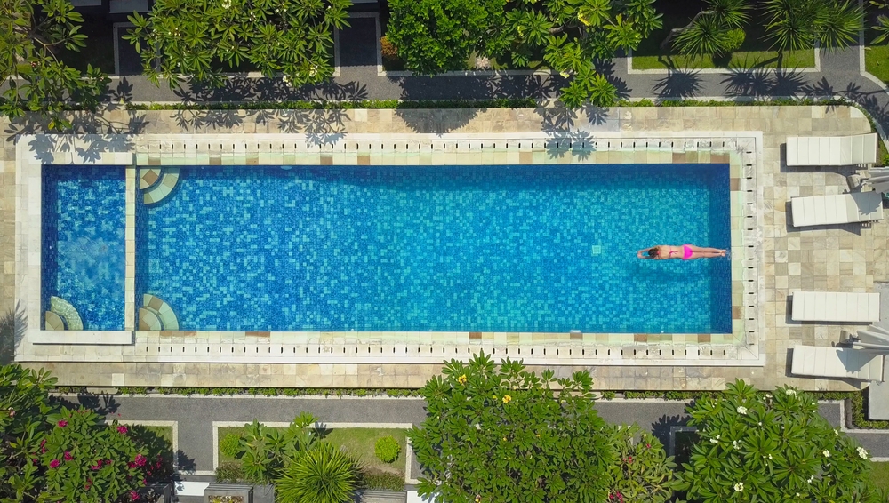 Unrecognizable female tourist in pink bikini dives into epic pool in luxury tropical island resort.