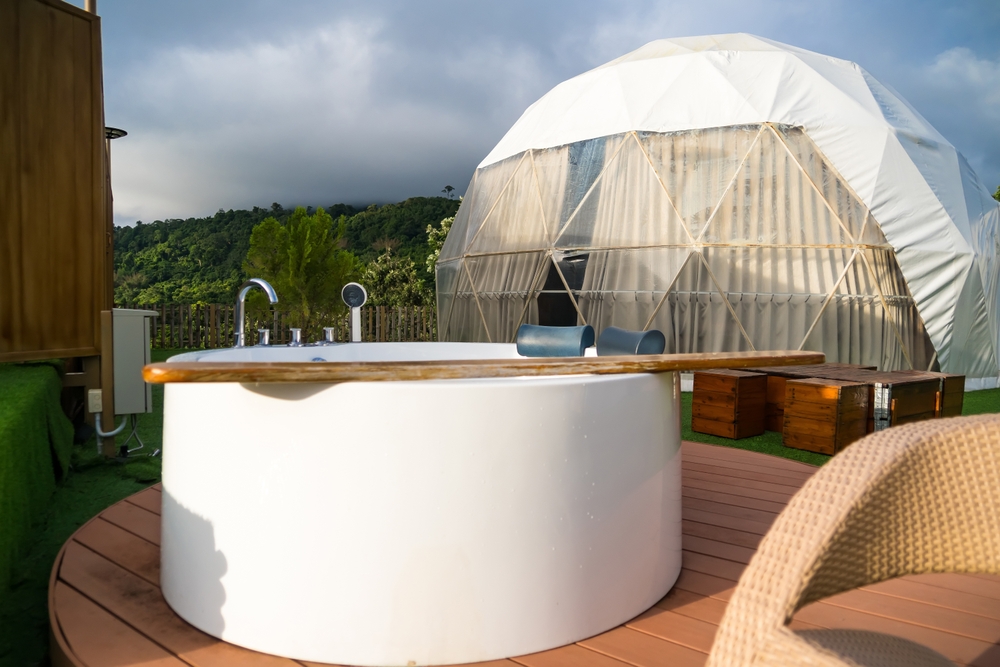 a modern geodesic dome tent situated on a lush green lawn, under a vast blue sky punctuated by fluffy white clouds.