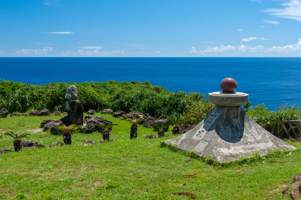 Japan Westernmost point monument. A monument on green grass, coastal vegetation, blue sky, deep blue ocean on the background. Yonaguni Island