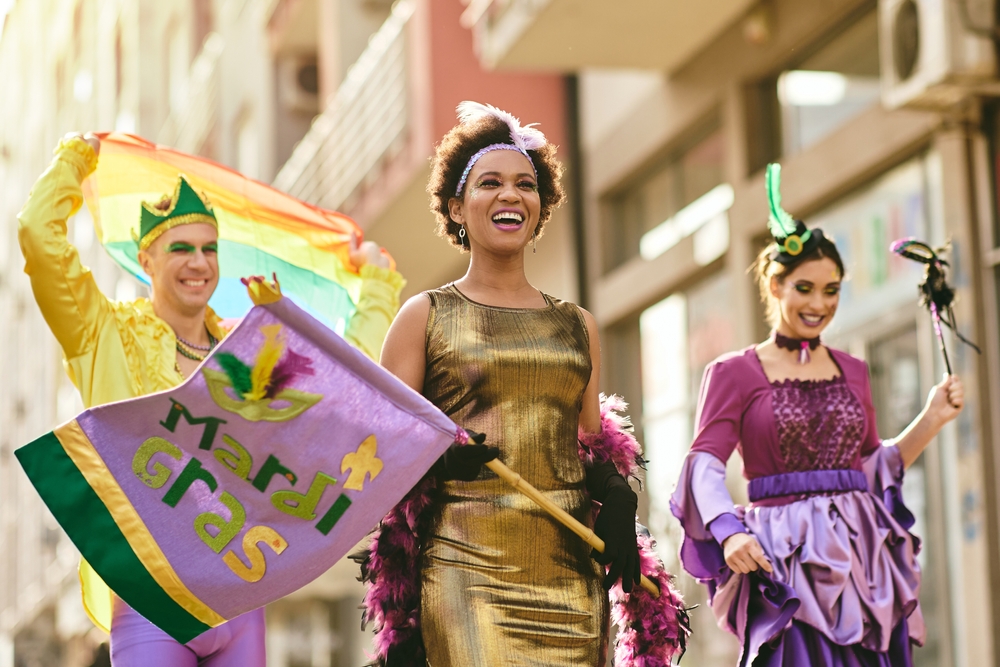 Happy African American woman and her friends in carnival costumes and make-up on Mardi Gras parade.