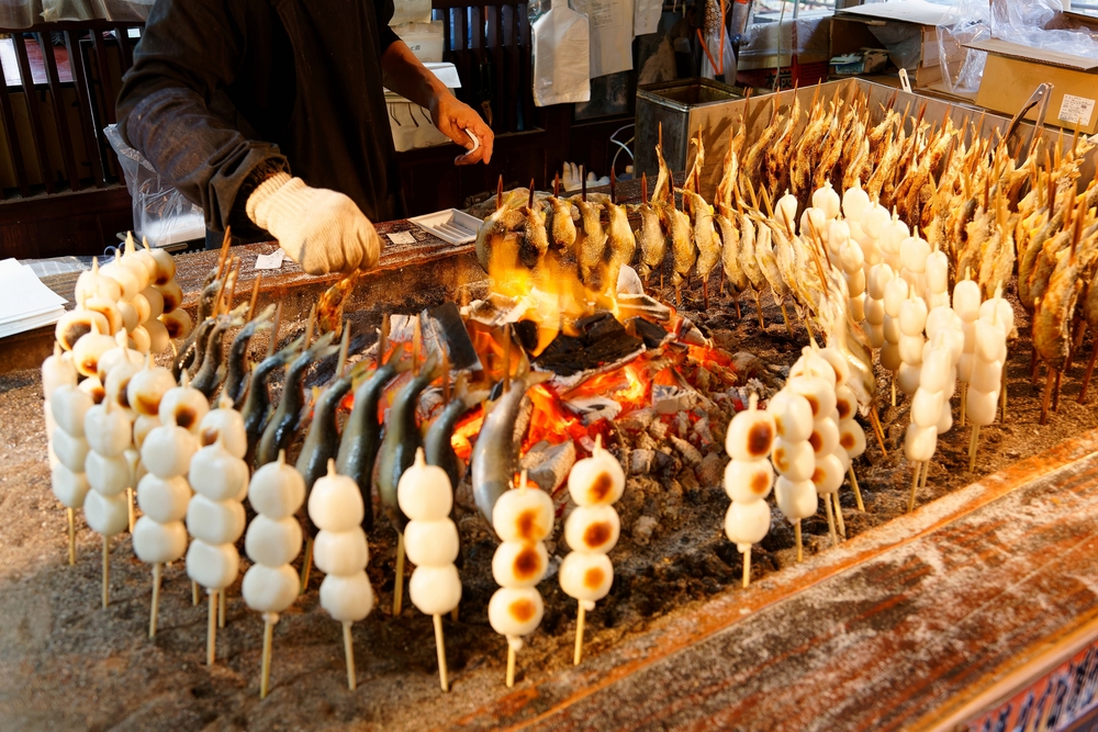 Around a charcoal fire, a stall vendor roasting skewered Iwana fish and Kushi Dango, which is made from rice flour and a street-food popular with Japanese people (in Yumoto, Oku-Nikko, Tochigi, Japan)