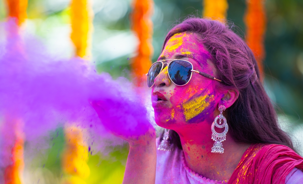 Young indian girl with sunglasses blowing holi colour powder from hand