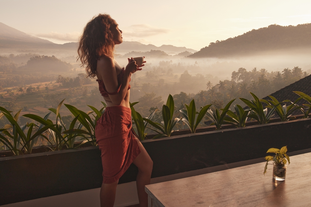 Woman enjoys a peaceful sunrise retreat with a cup of coffee, overlooking stunning views in Bali. 