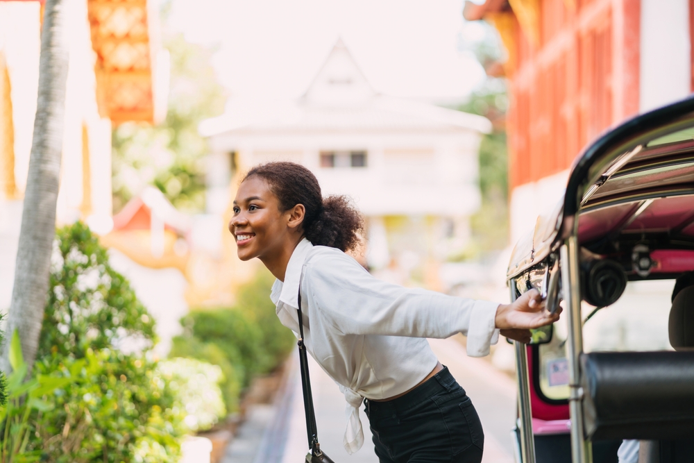 happy black traveler girl hang out from tuk tuk ride. african american young tourist using bar hang out for air on ride tuk tuk.