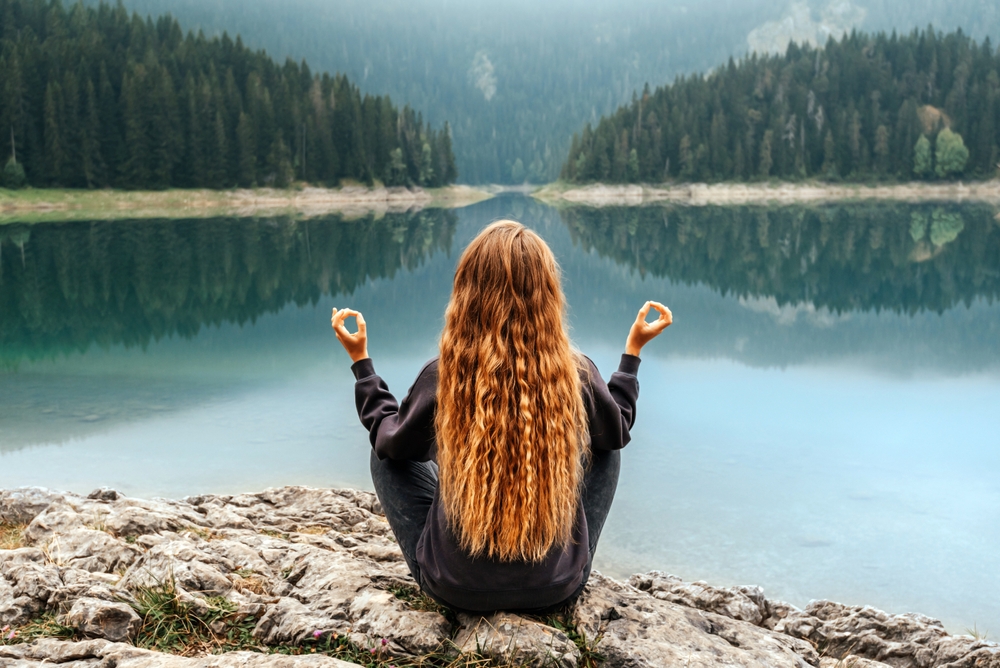 Woman meditating alone on shore of mountain lake. 