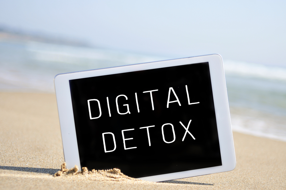 a tablet computer with the text digital detox written in its screen, placed in the sand of a beach