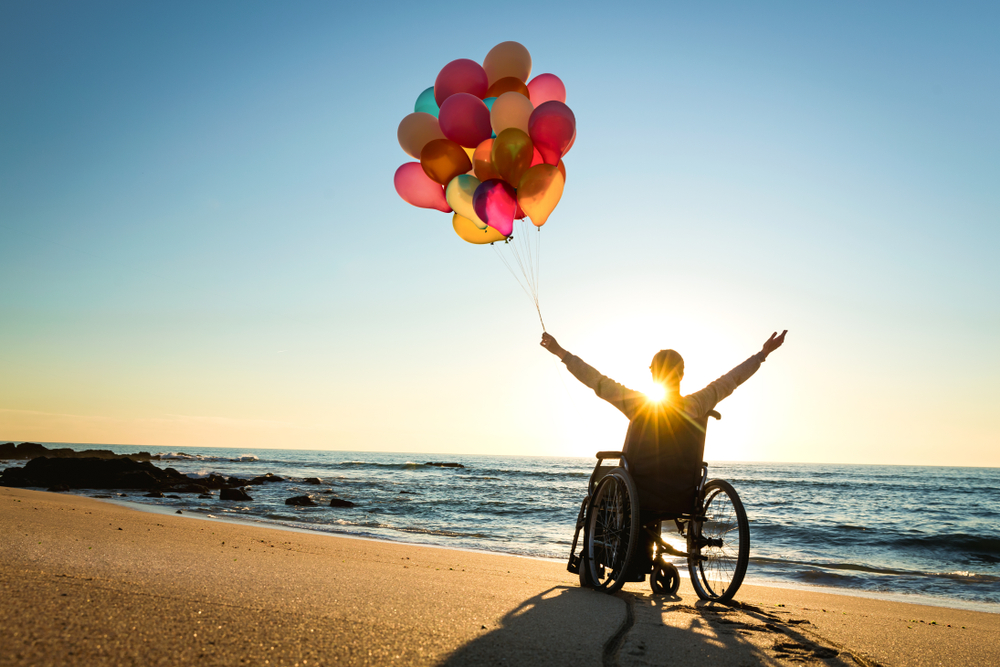 Handicapped man on a wheelchair with colored balloons at the beach