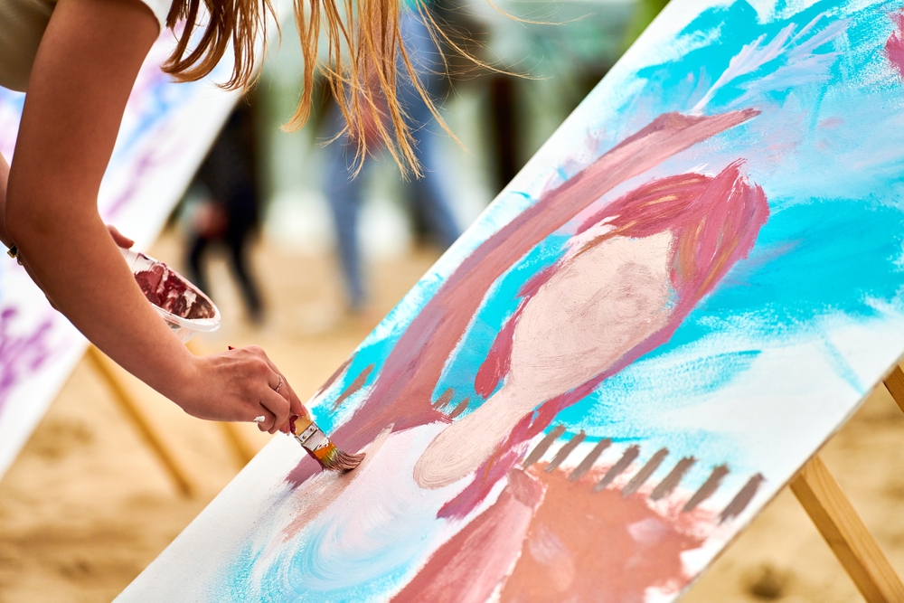 Amateur painter draws picture on white canvas at outdoor art workshop. Woman artist hands with paintbrush painting new picture, outdoor art exercise, painting performance