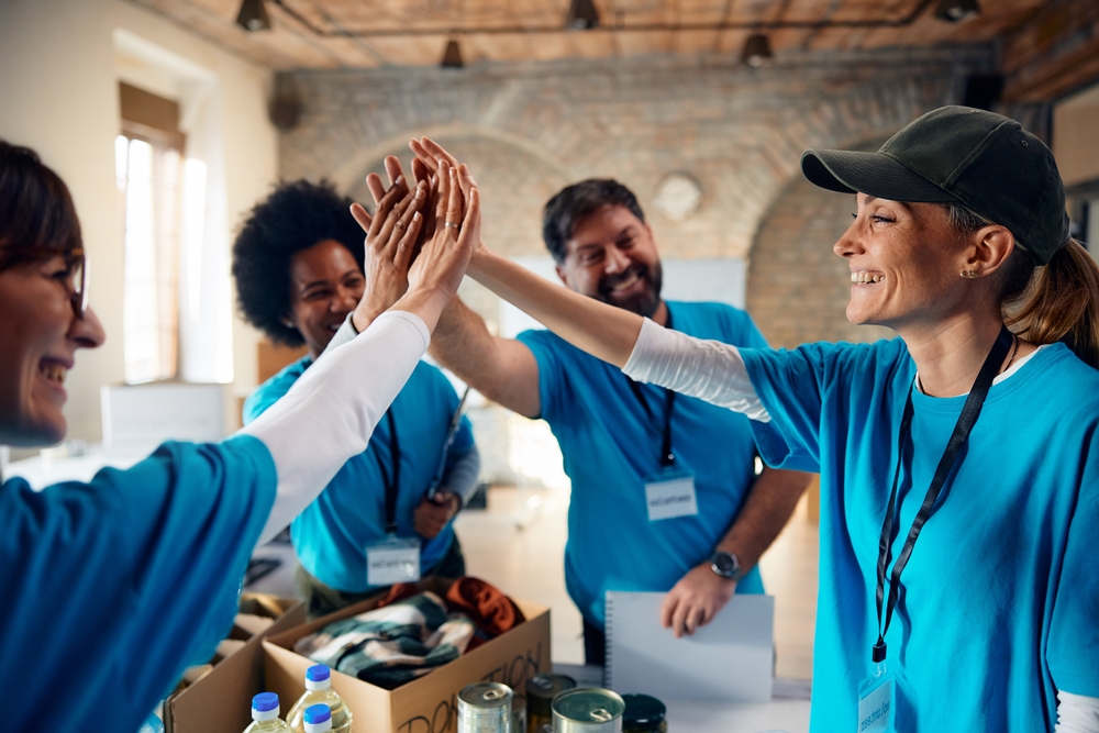 Group of happy volunteers gathering hands in unity while working at charitable foundation.