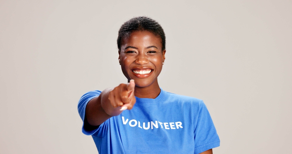 Happy, black woman or volunteer with finger pointing to you for choice or selection on a white studio background. 