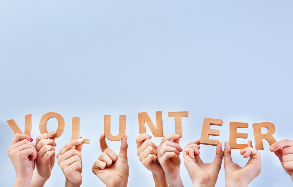 People putting hands in air together with word made of wooden letters on light background. Volunteering concept