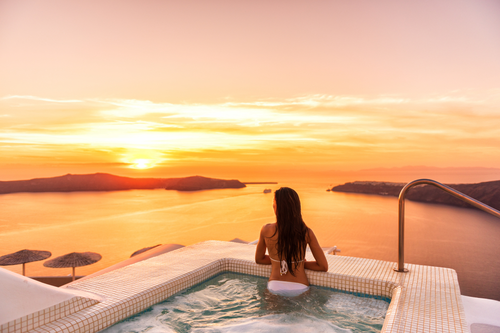 Luxury travel Santorini vacation woman swimming in hotel jacuzzi pool watching sunset