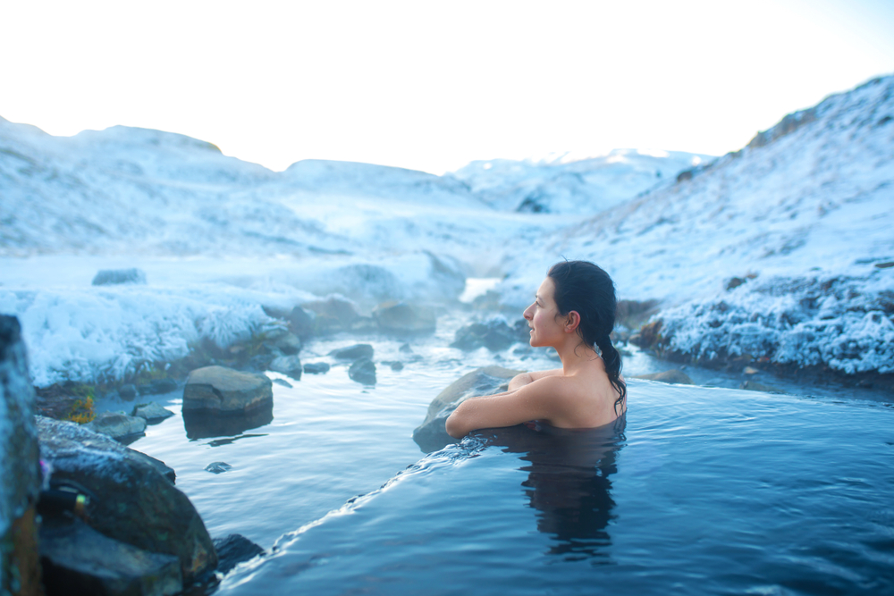 The girl bathes in a hot spring in the open air with a gorgeous view of the snowy mountains.