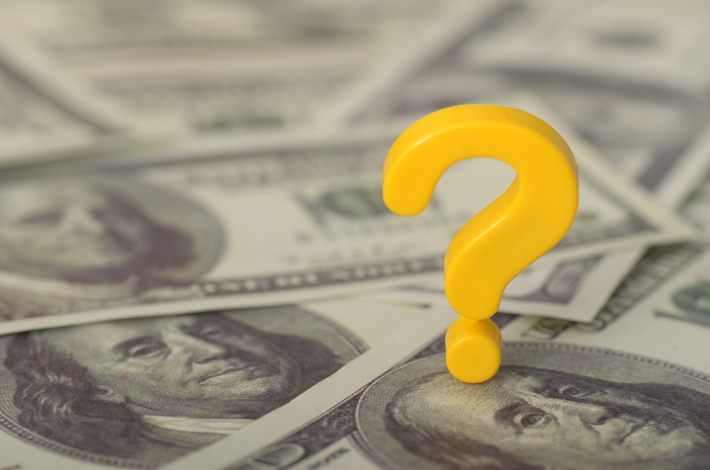 The image depicts a yellow question mark resting on a bed of 100-dollar bills, symbolizing uncertainty and confusion surrounding financial matters.