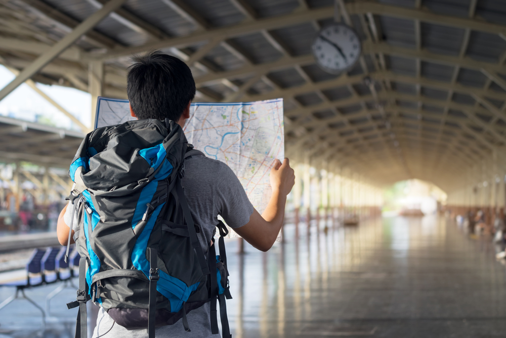 Asia man holding map with bag backpack alone in the train station, preparing,planing and find location for travel trip.