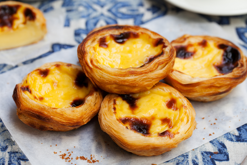 Egg tart, traditional Portuguese dessert, pastel de nata on a plate. Blue textile background.