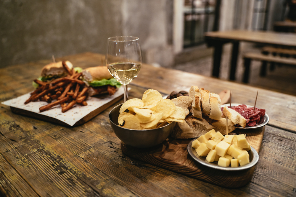 Meal for two in a rustic restaurant in the LX Factory complex in Lisbon, Portugal with sliced salami, cheese, olives, chips , baguette sandwich and glass of white wine