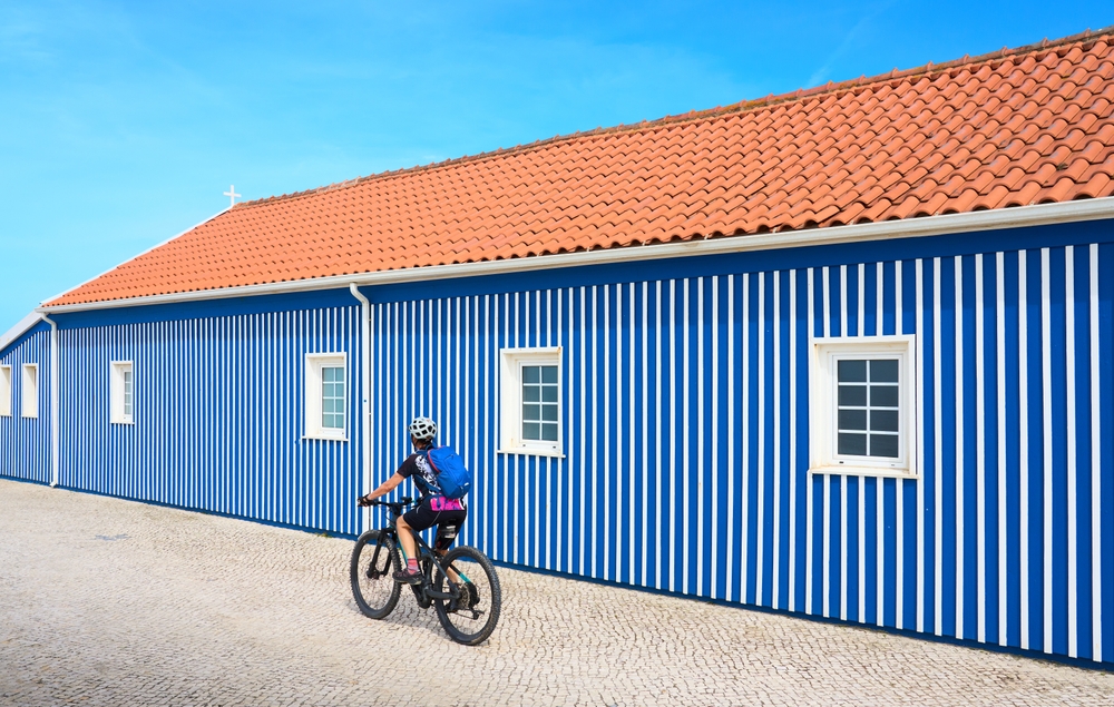 nice woman cycling with her electric mountain bike in front of the colorful wooden houses of Costa Nova do Prado near Aveiro, Portugal