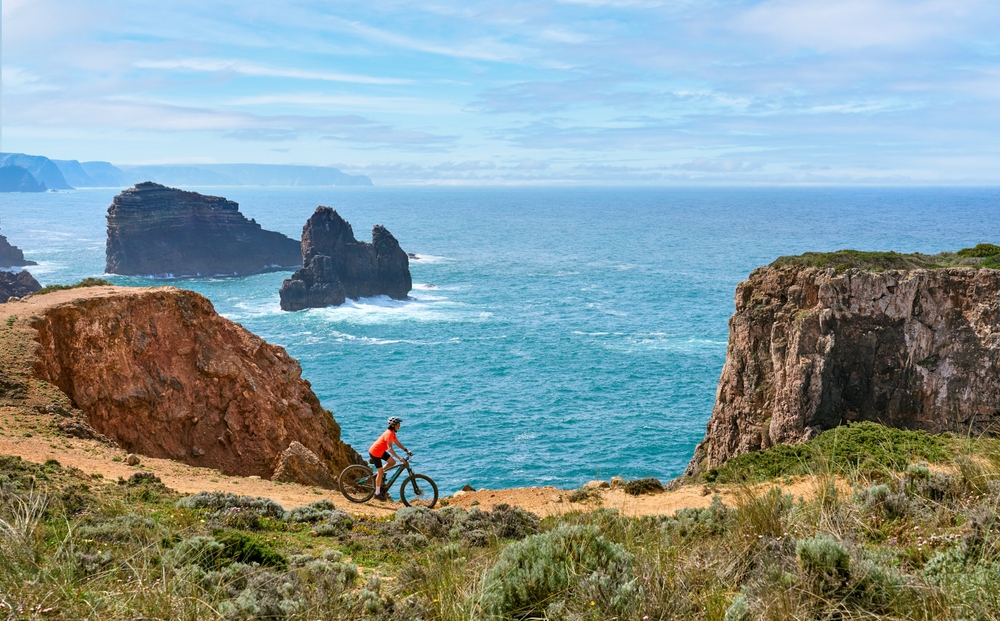 happy active senior woman cycling on the the rocky cliffs of the Vicentina coast of Portugal near Sagres and Vila do Bispo
