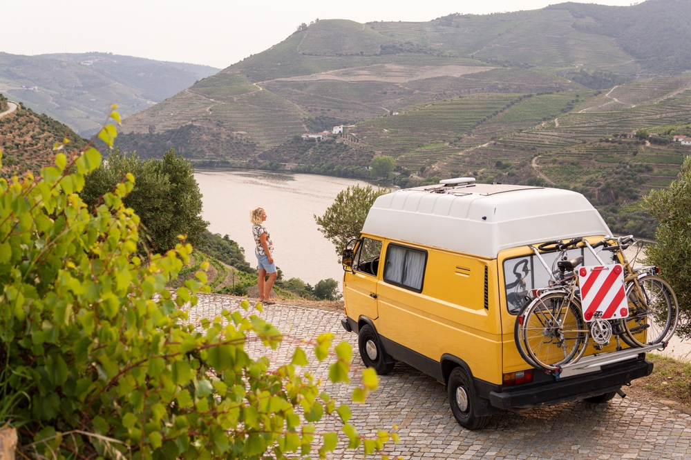 Blonde woman enjoying the view standing by her retro camper van parked in Douro valley, Portugal