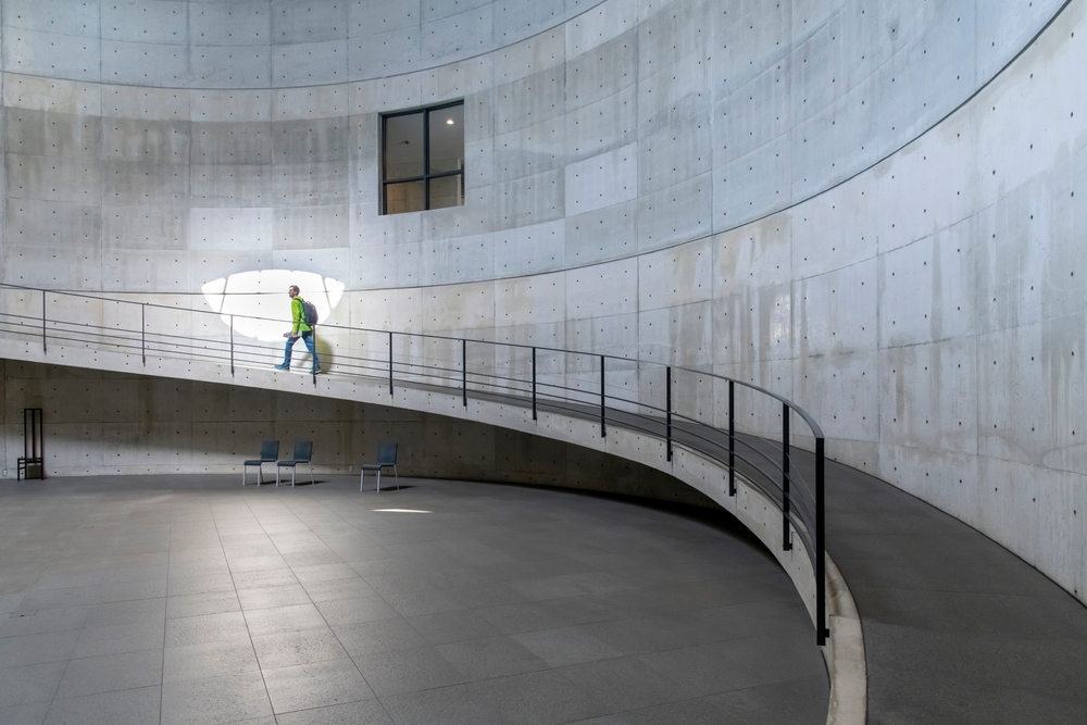 Interior view circular walkway with one person against the fair faced concrete walls of the Benesse House contemporary art museum designed by Tadao Ando