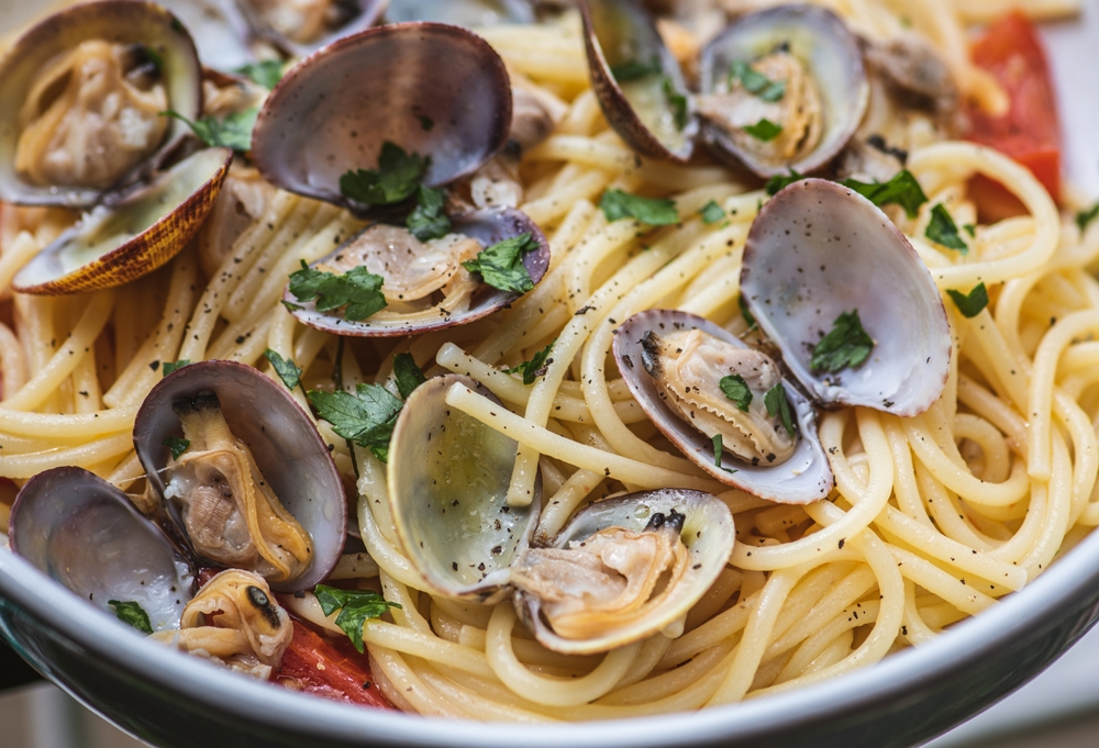 Spaghetti with clams, fresh cherry tomatoes, parsley leaves and ground black pepper, close up