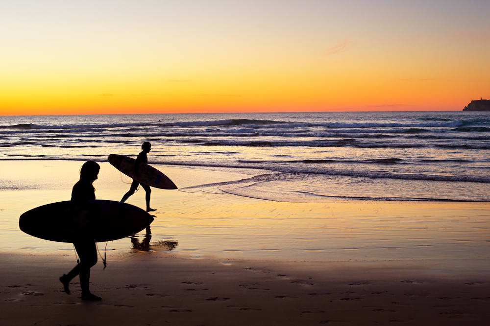 Two surfer running on the beach at sunset.