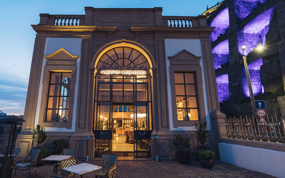 Elegant Vincci Ponte de Ferro boutique hotel facade featuring neoclassical design with illuminated Dom Luis Bridge background