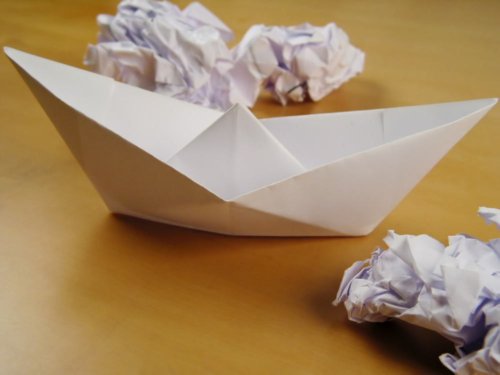 Close-up of a paper-boat cruising through wads on desk