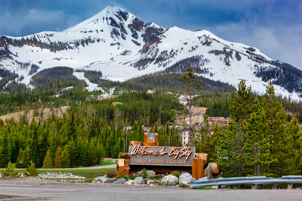 Welcome to Big Sky Mountain Village Signage, dwarfed by the enormity of Lone Mountain full of snow in the Madison Range in the state of Montana USA.