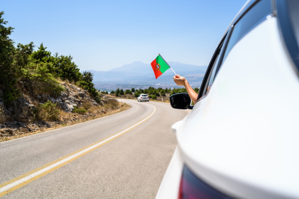Woman holding Portugal flag from the open car window driving along the serpentine road in the mountains.