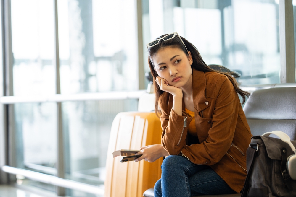 Unhappy young woman traveler disappointed with flight delay or cancelation while waiting at airport terminal, female tourist upset after receiving bad news when sitting at airline lounge.
