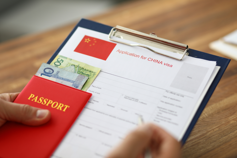 Male hand hold silver pen with passport. Filling China apllication form concept