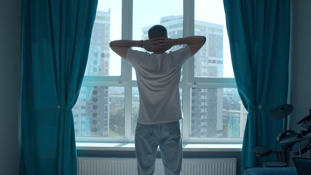 Early morning, a man at the window raising his hands and stretching.